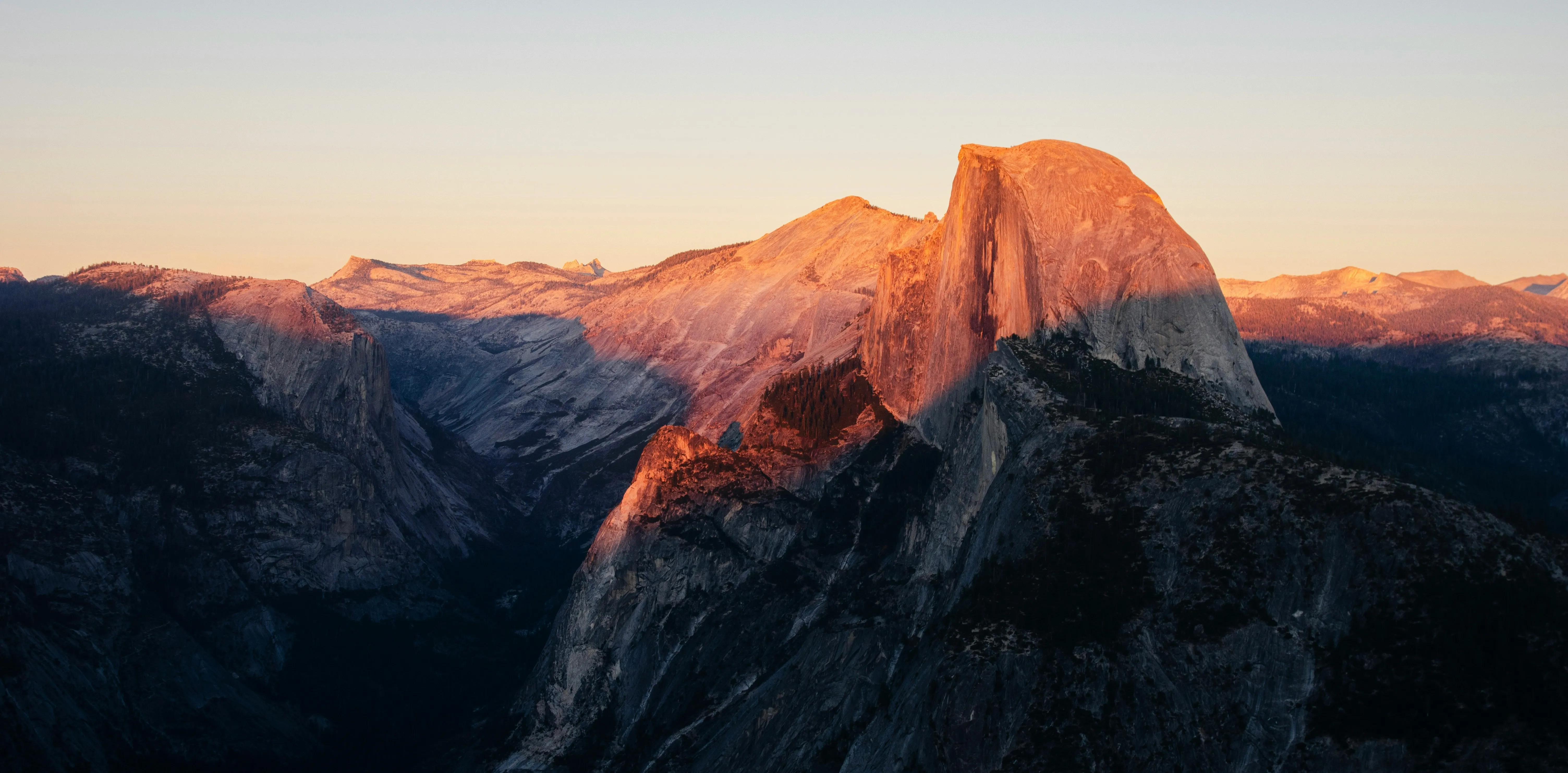 Half Dome's granite face glowing orange at sunset, seen from Glacier Point, backed by the High Sierra.