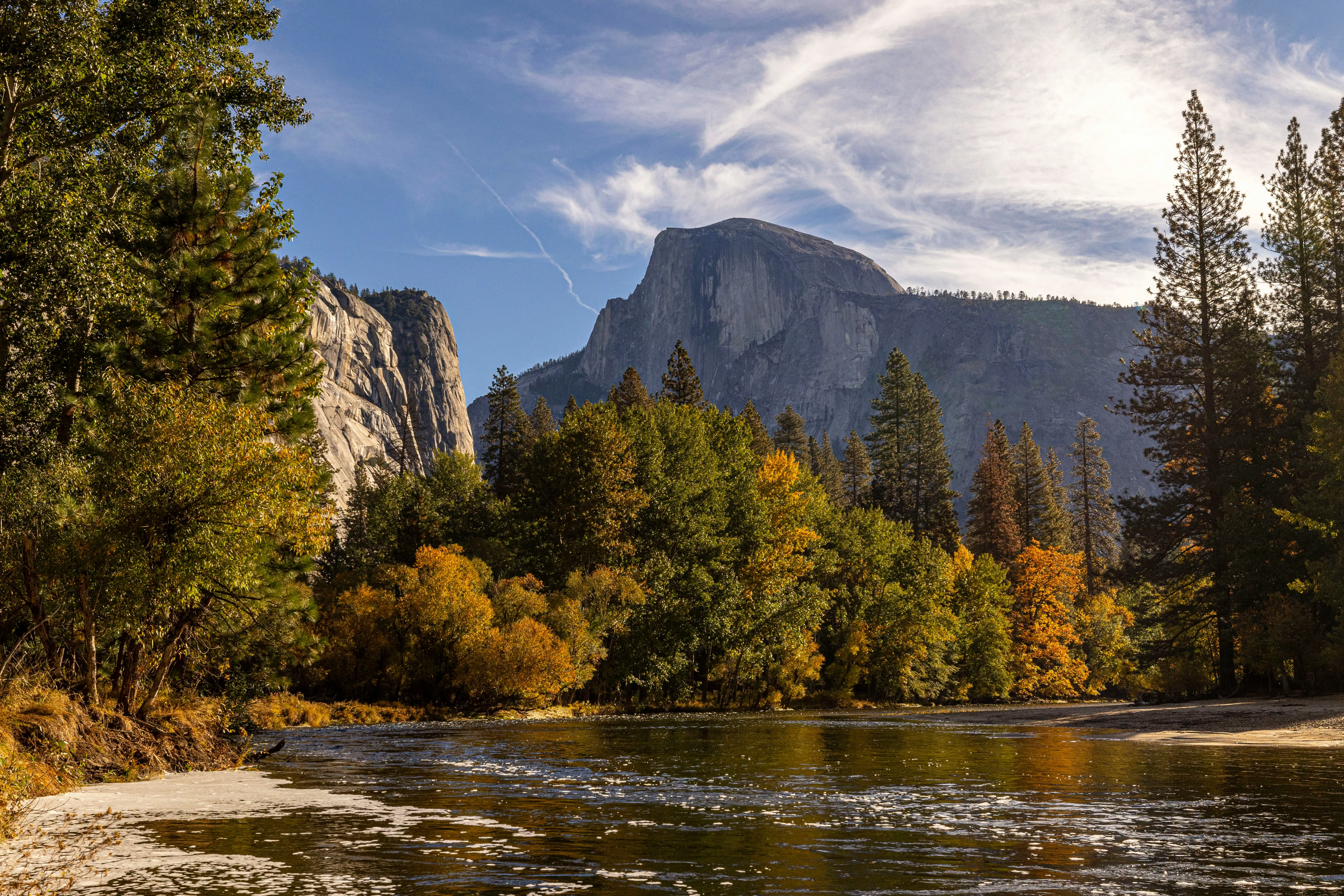 The Merced River in Yosemite Valley in autumn, Half Dome rising behind gold-and-green cottonwoods along the bank.
