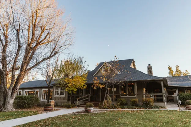 Sierra Sky Ranch's ranch building and wraparound veranda at dusk, framed by autumn trees.