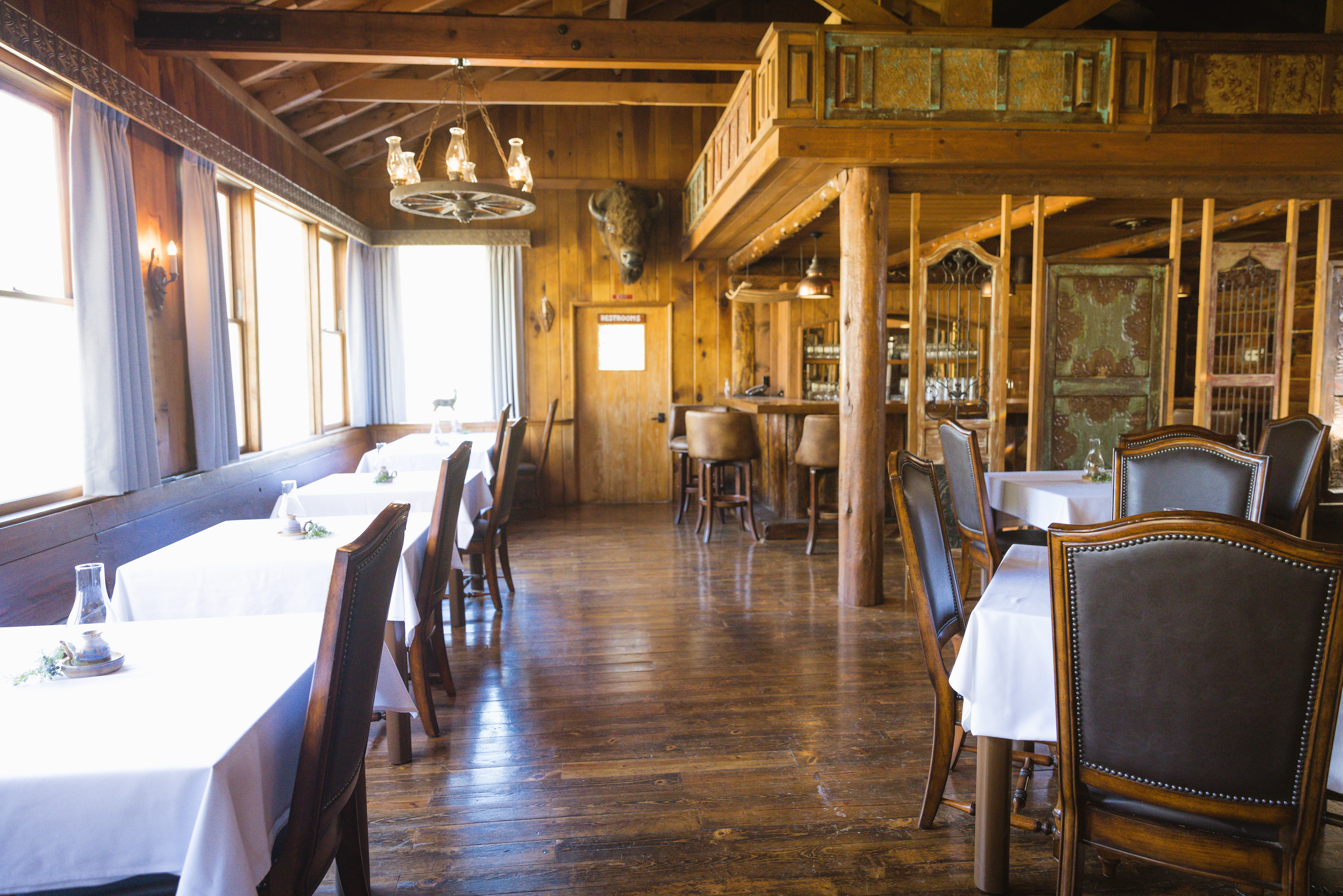 The rustic dining room at Sierra Sky Ranch, with a beamed ceiling, antique fixtures, and white-clothed tables.