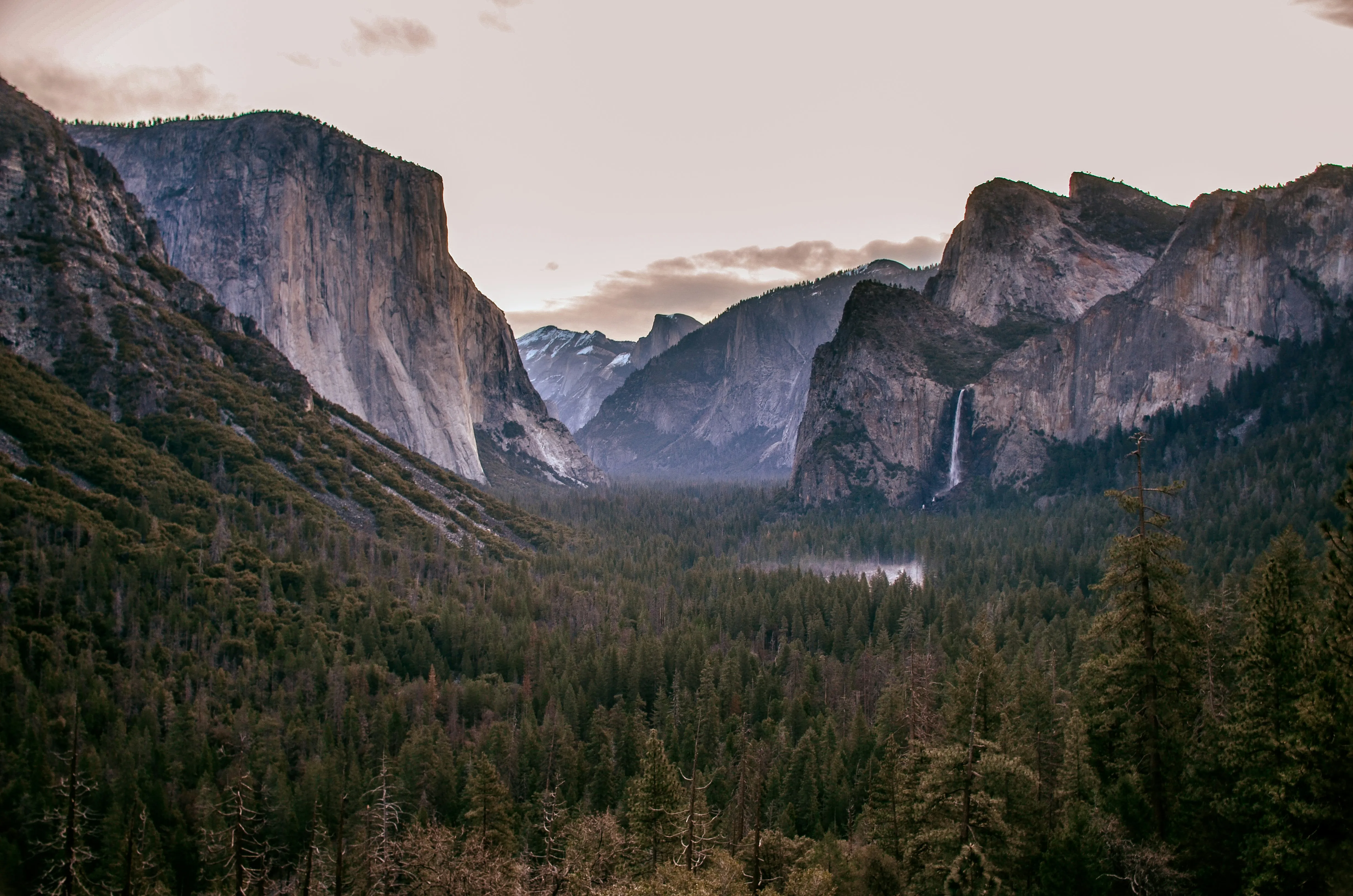 Tunnel View: El Capitan at left, Half Dome in the center distance, Bridalveil Fall at right, above the forested valley.