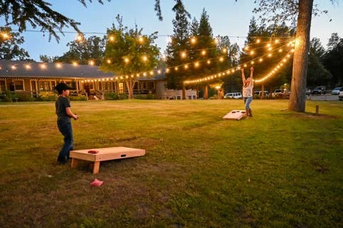 Sierra Sky Ranch, corn hole on the Great Lawn at dusk, lights strung from the trees overhead.